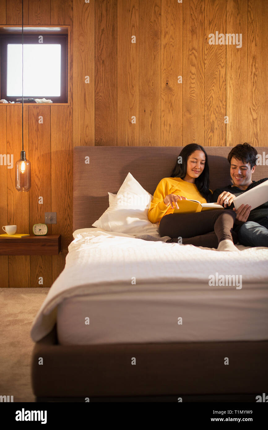Couple reading book and using digital tablet in bed Stock Photo