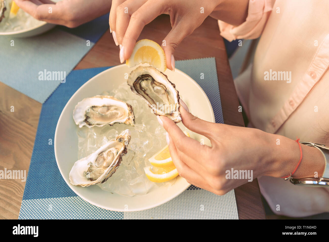 Accurate woman carrying opened oyster and adding lemon juice Stock