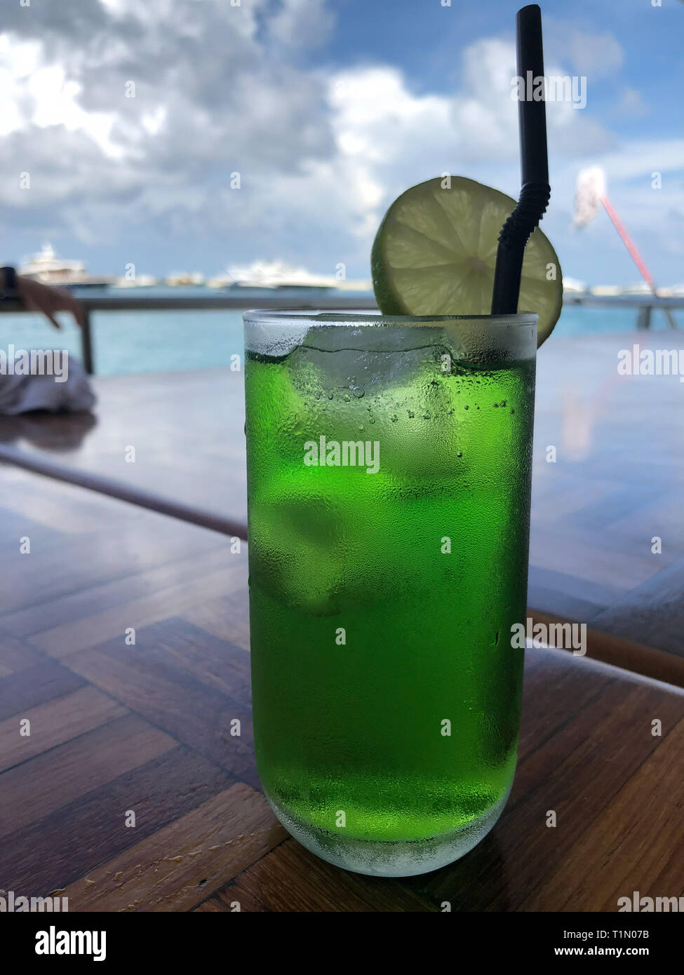 Closeup of green tropical drink sitting on seaside bar top with slice ...