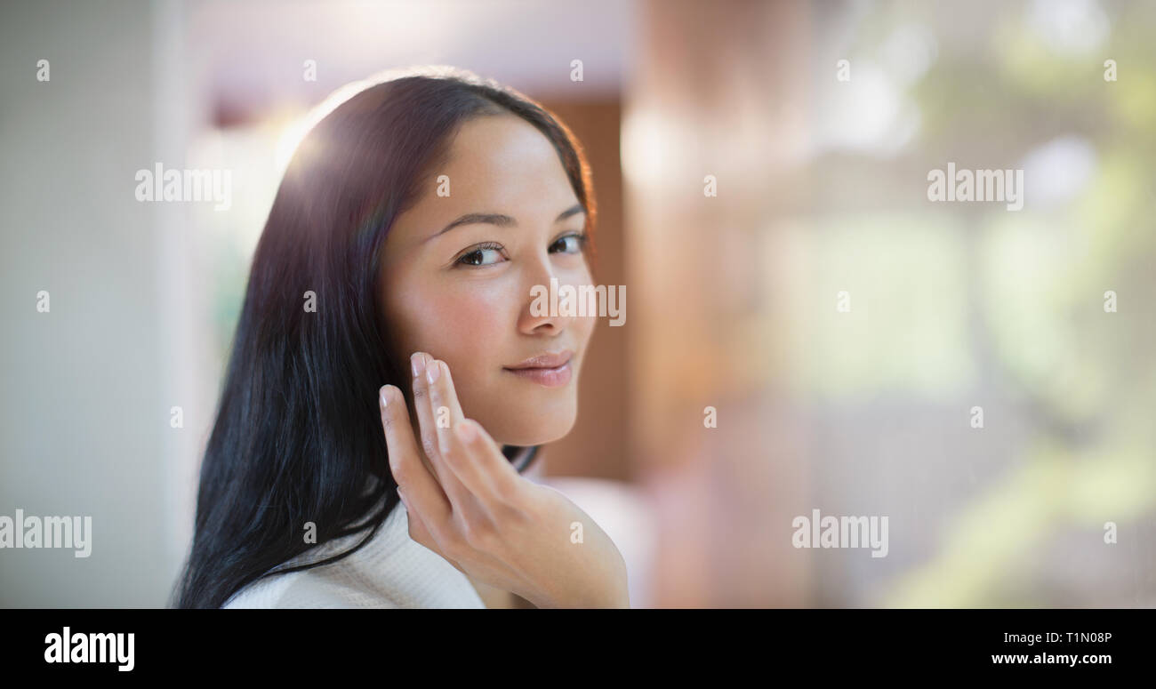Portrait confident young woman applying moisturizer to face Stock Photo