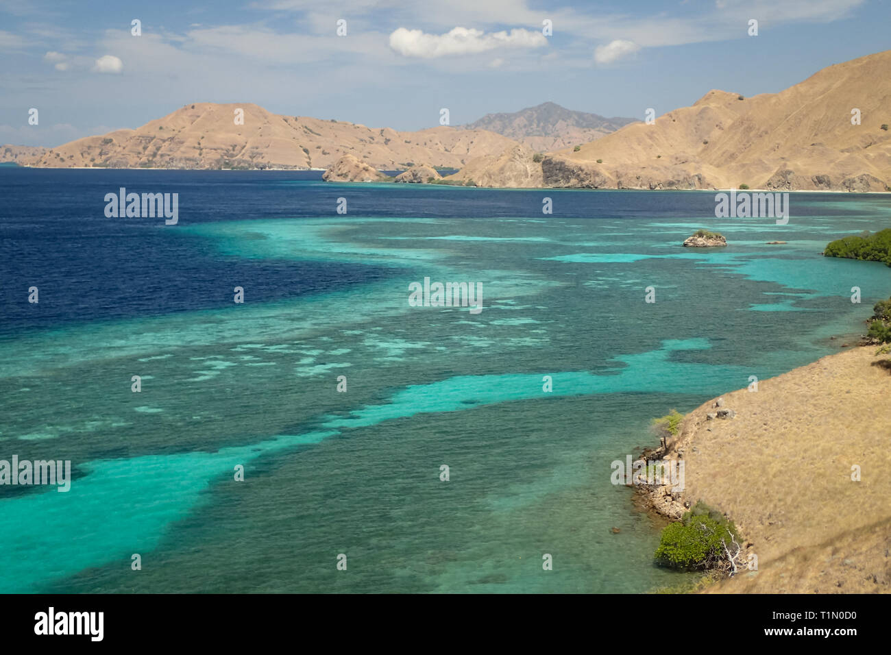 Arid barren  mountains of Nusa Tenggara Timur surrounded by coral reef and blue tropical waters Stock Photo