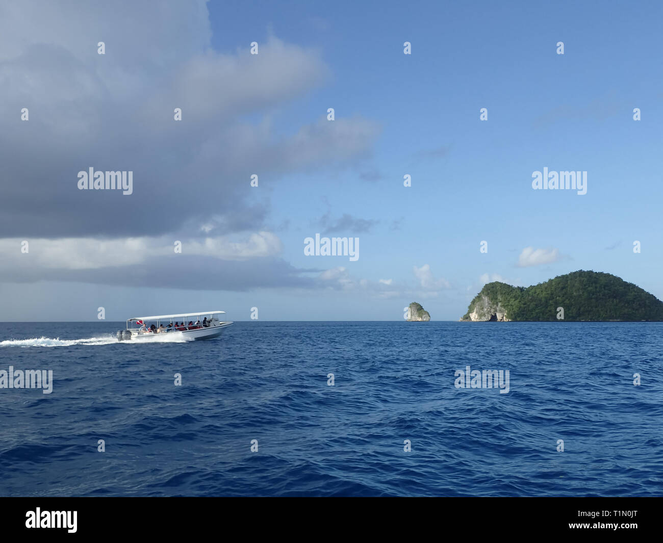 A boat full of people is speeding across the water towards a small ...