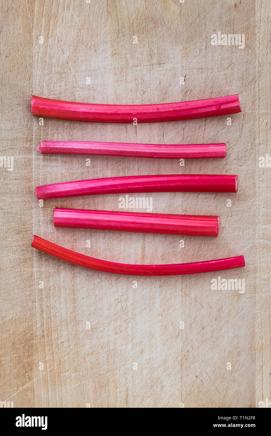 Forced pink rhubarb stalks on wooden chopping board Stock Photo