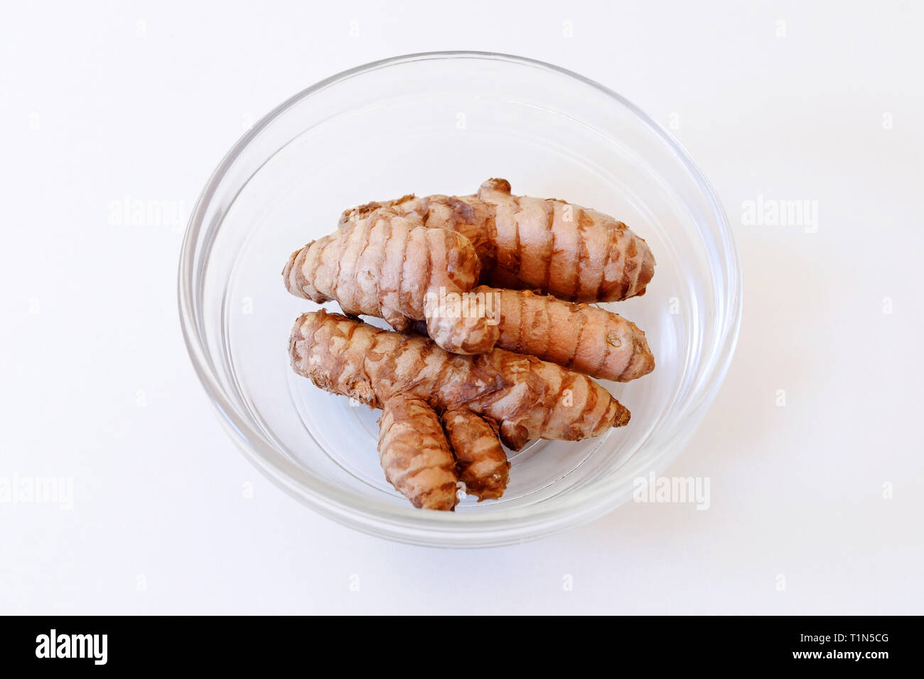 Turmeric, tuber, intact root. Single ingredient in glass bowl isolated