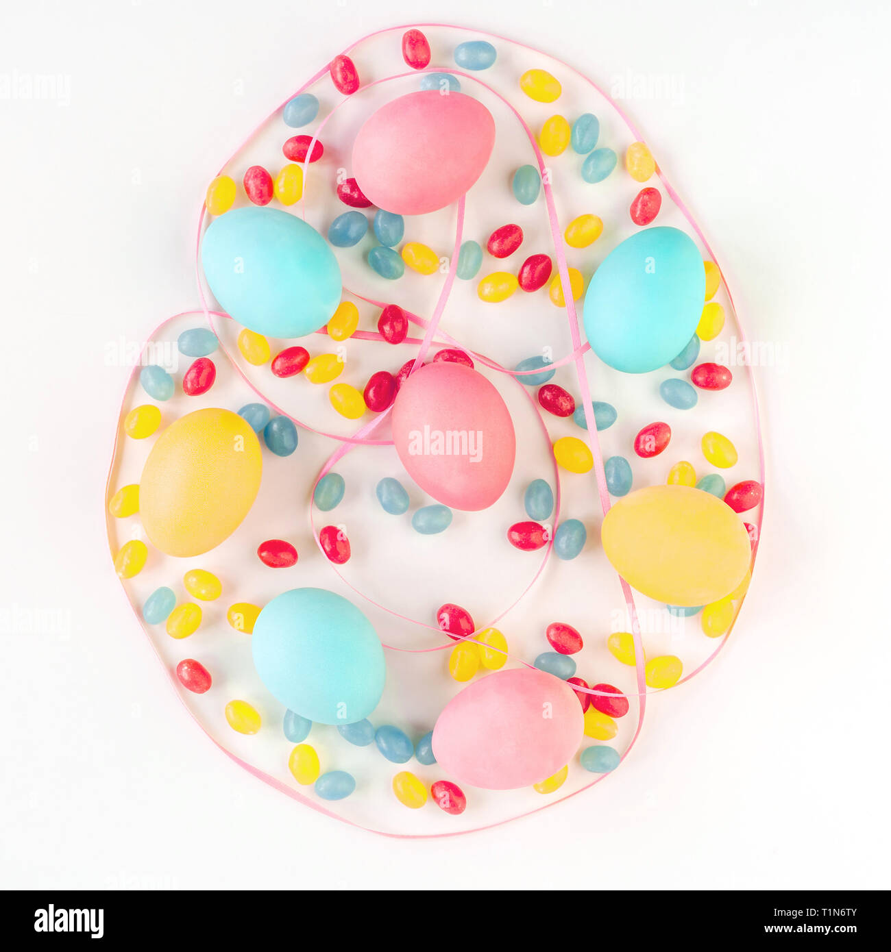 Colorful Easter egg concept. Easter eggs and candies with pink satin ribbon on isolated white background. Flat lay. Stock Photo