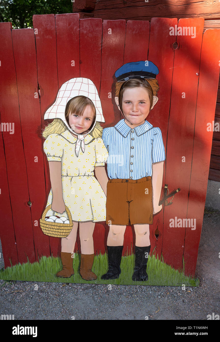 Two girls faces in a face hole board with a painted picture of old fashioned boy and girl. Stock Photo