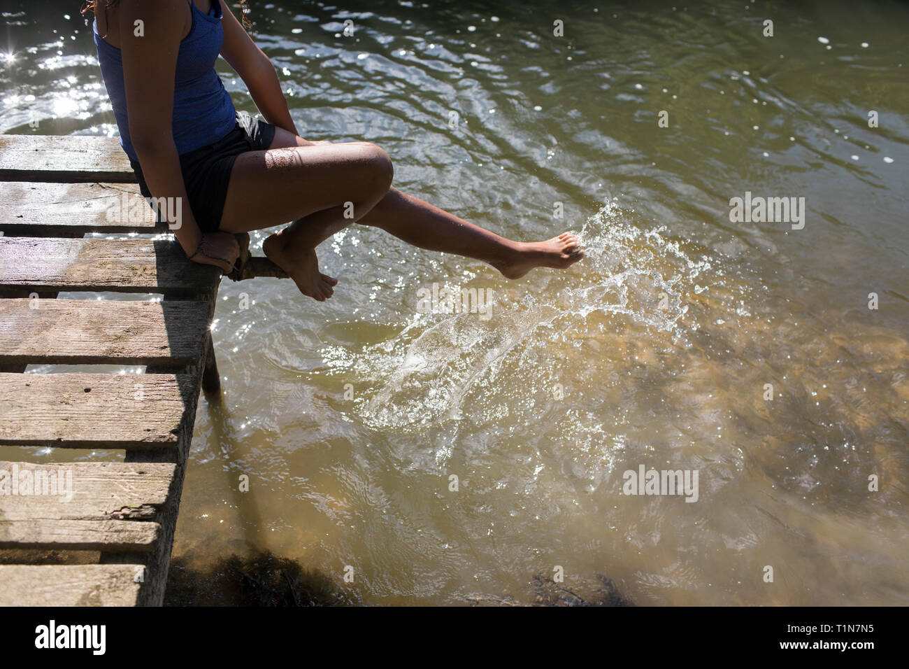Girl on sunny dock splashing foot in river water Stock Photo