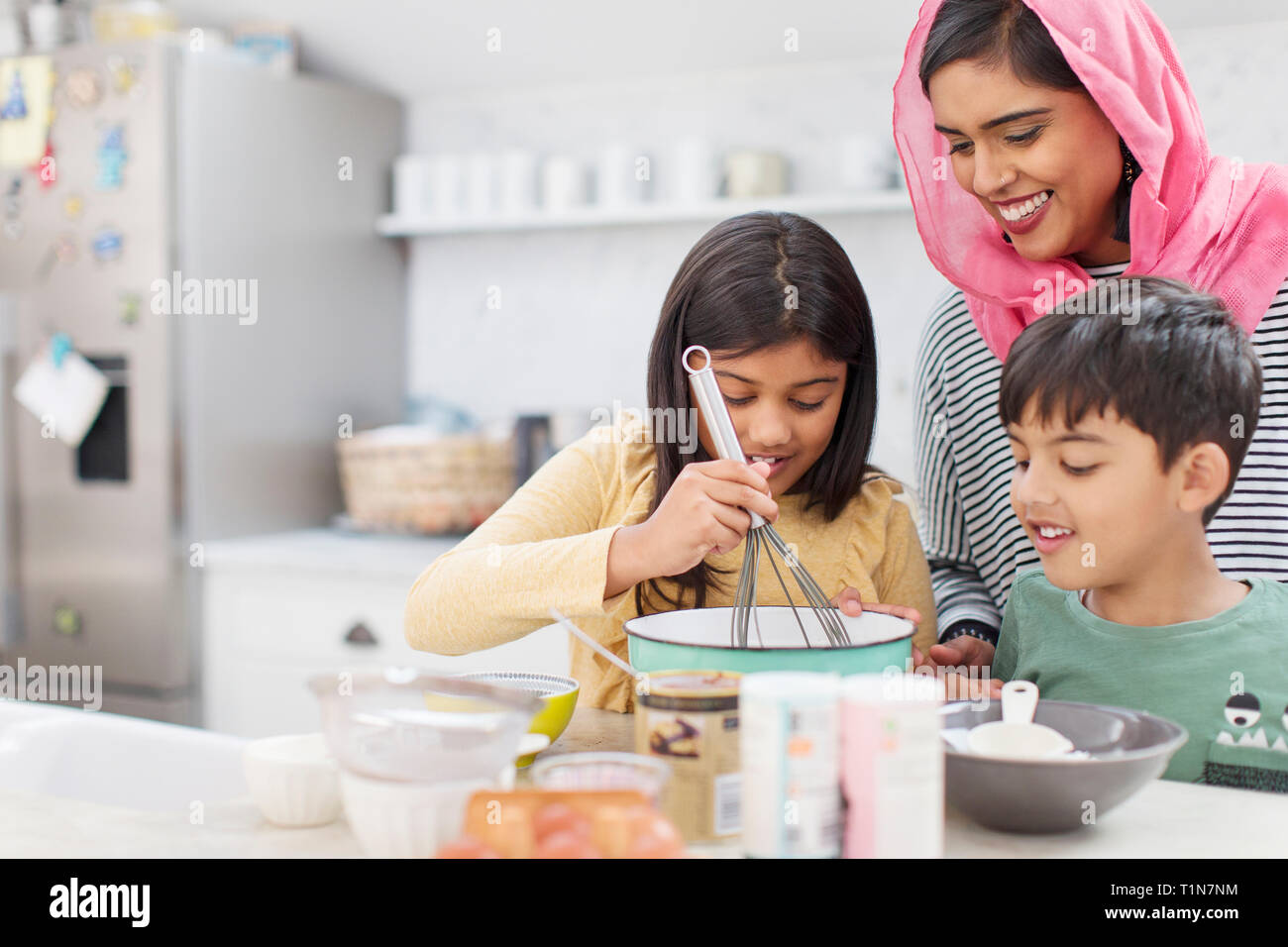 Mother in hijab baking with children in kitchen Stock Photo