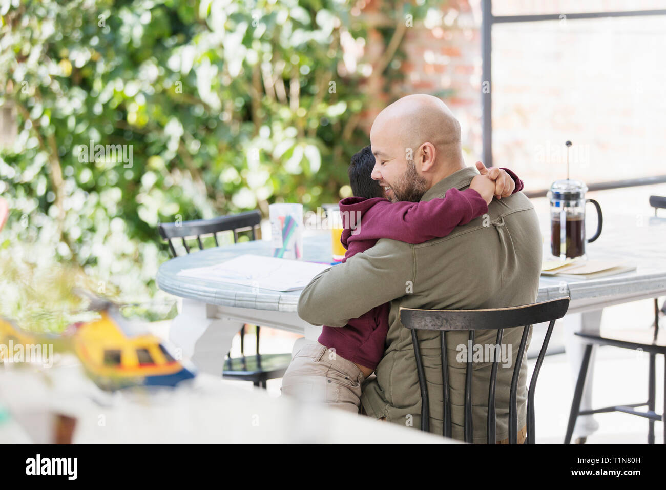 Affectionate father and son hugging at table Stock Photo