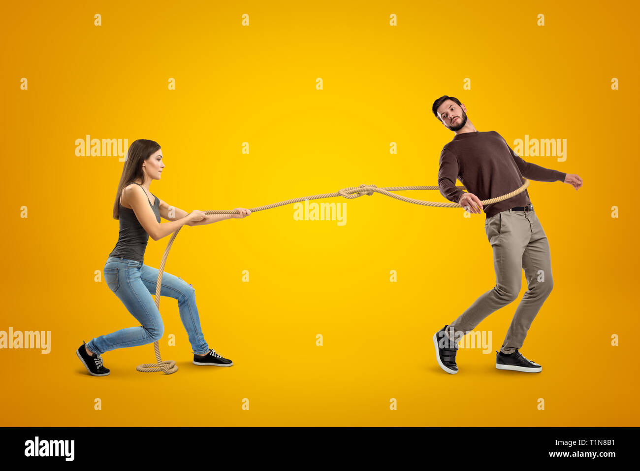 Side view of young woman lassooing young man on yellow background. Stock Photo