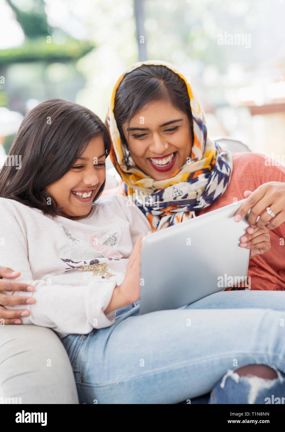Laughing, happy mother in hijab and daughter using digital tablet Stock Photo