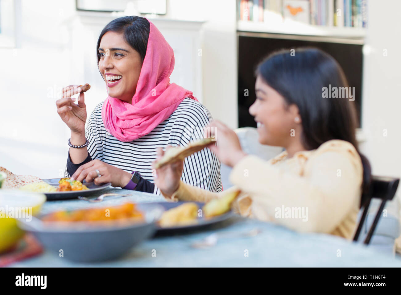 Happy mother in hijab and daughter eating dinner Stock Photo