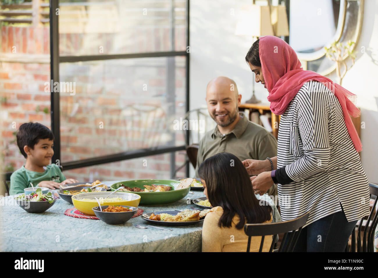 Mother in hijab serving dinner to family at dining table Stock Photo
