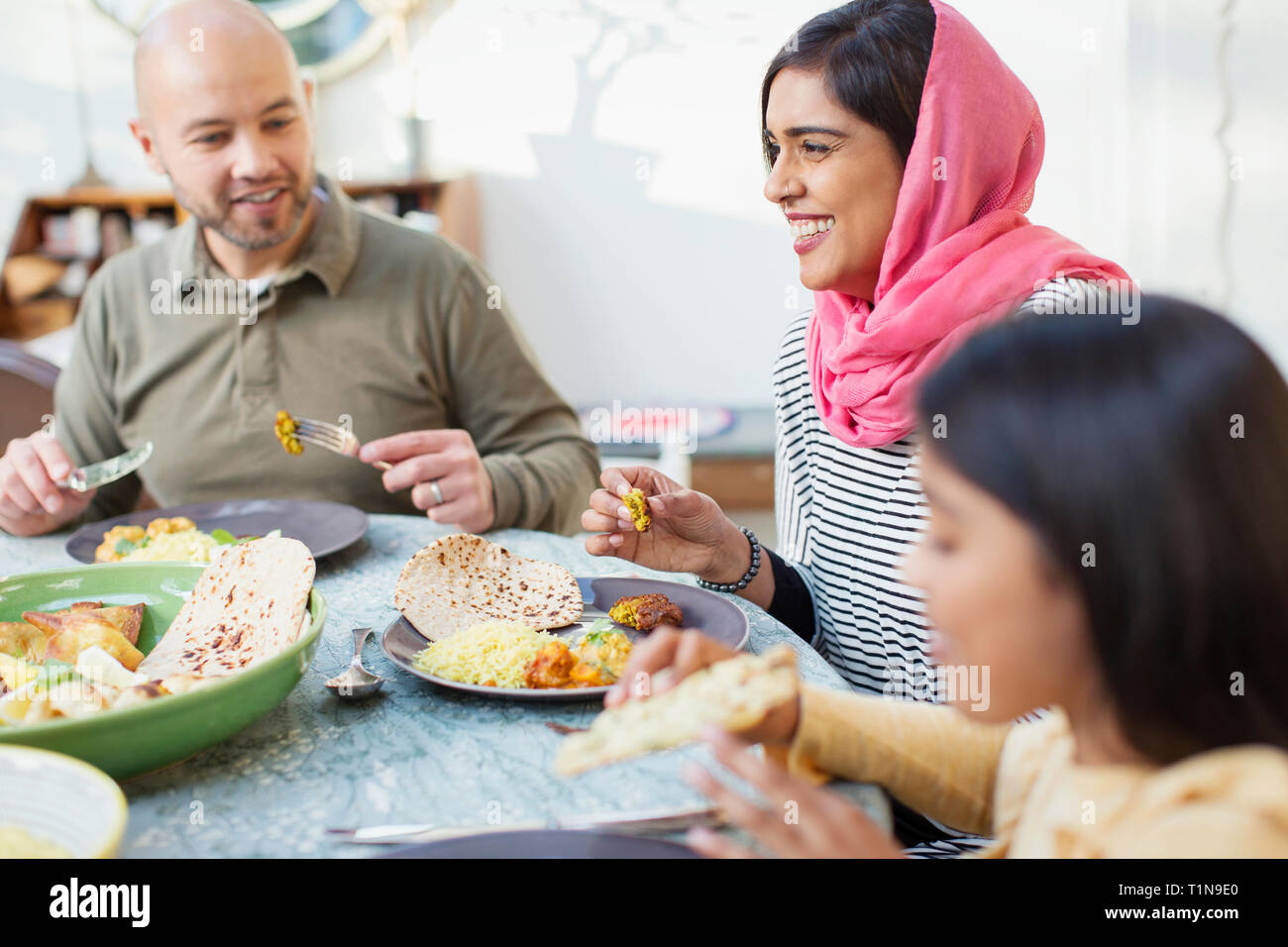 Happy woman in hijab eating dinner with family at table Stock Photo