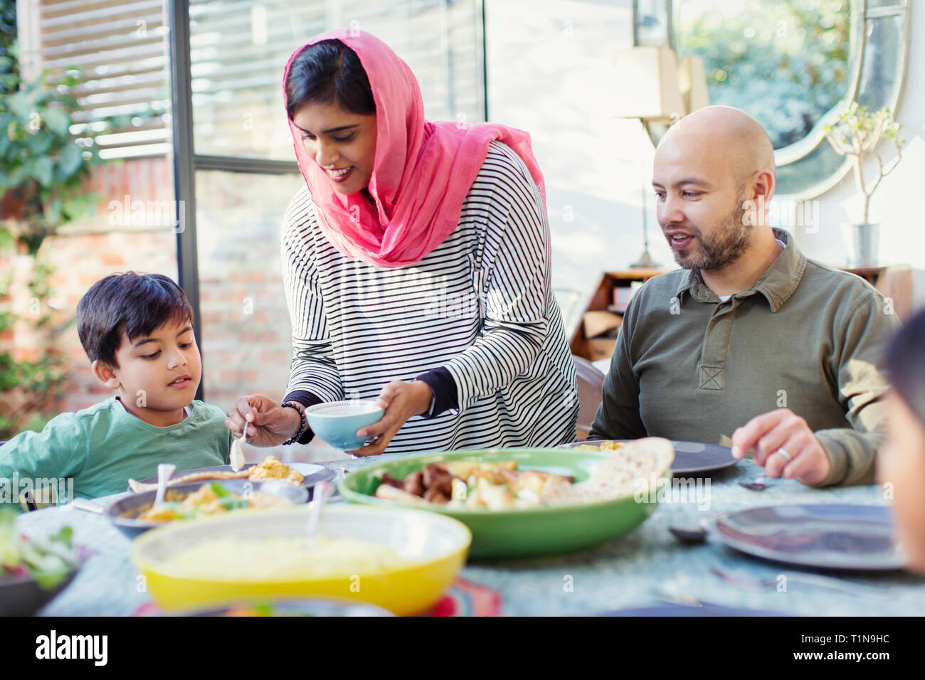 Mother in hijab serving dinner to family at table Stock Photo