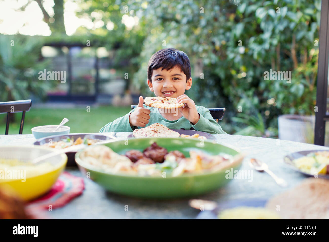 Portrait happy boy eating naan bread at patio table Stock Photo