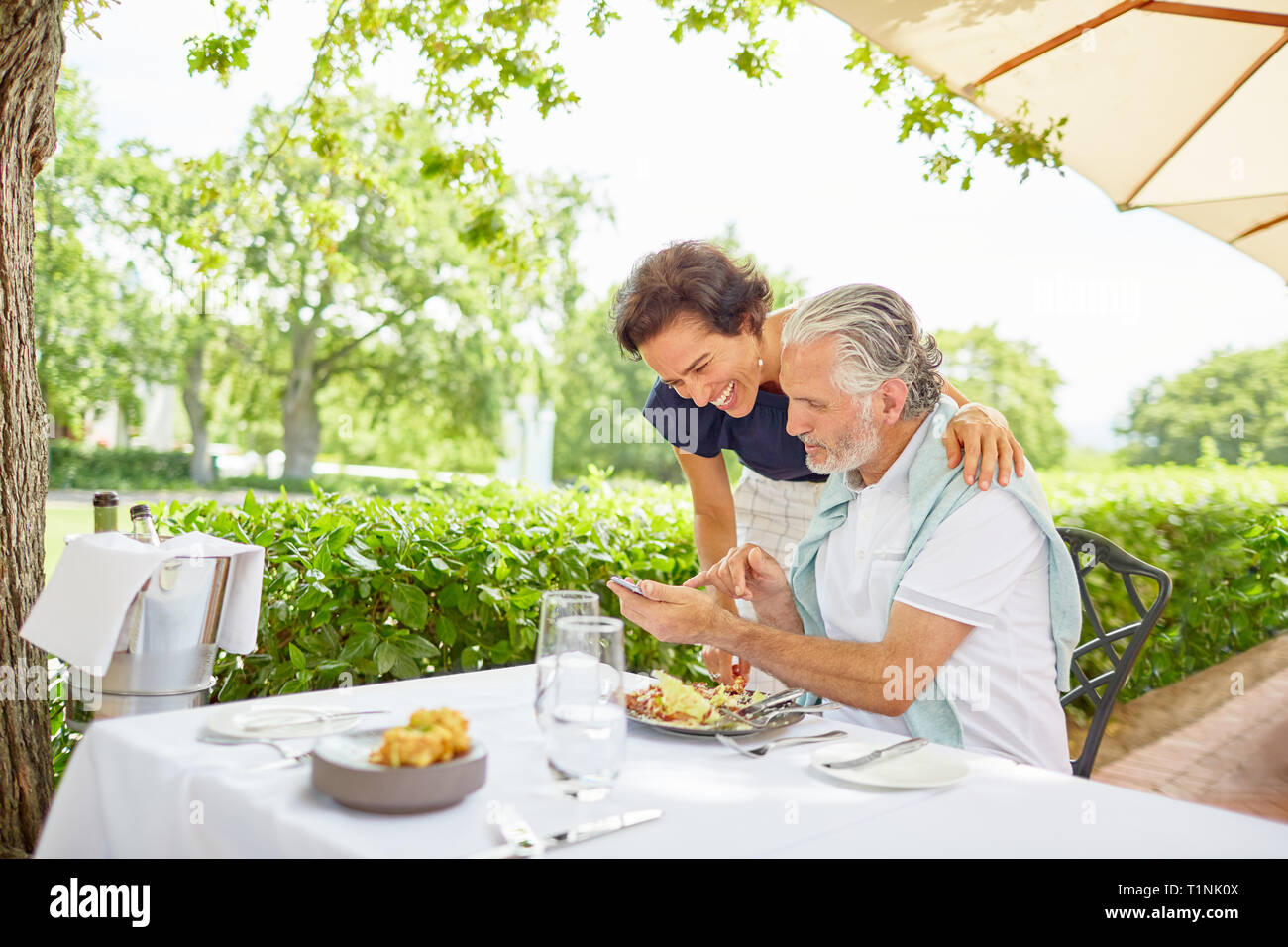 Mature couple dining, using smart phone at patio table Stock Photo