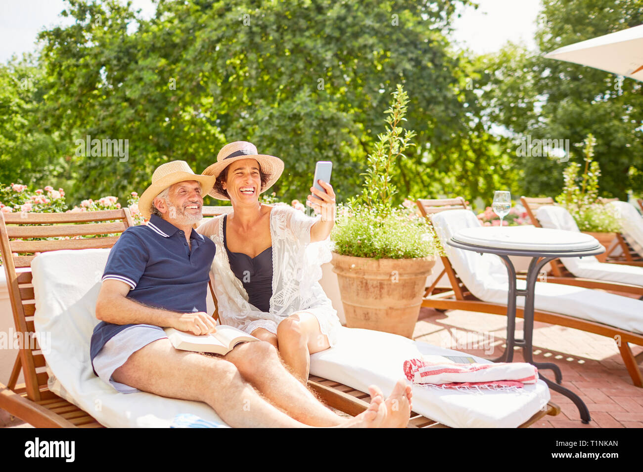 Happy mature couple taking selfie with camera phone at sunny resort poolside Stock Photo
