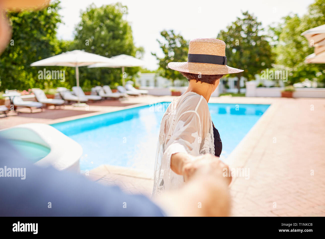 Mature couple holding hands at sunny poolside Stock Photo