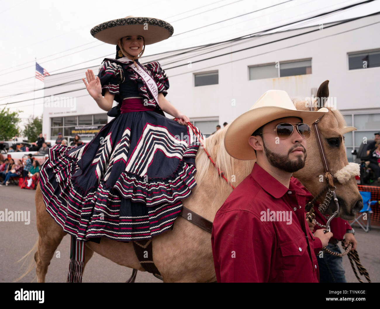 Young woman dressed in traditional charreada clothing waves while riding a horse in the annual Washington's Birthday Celebration parade in Laredo TX Stock Photo