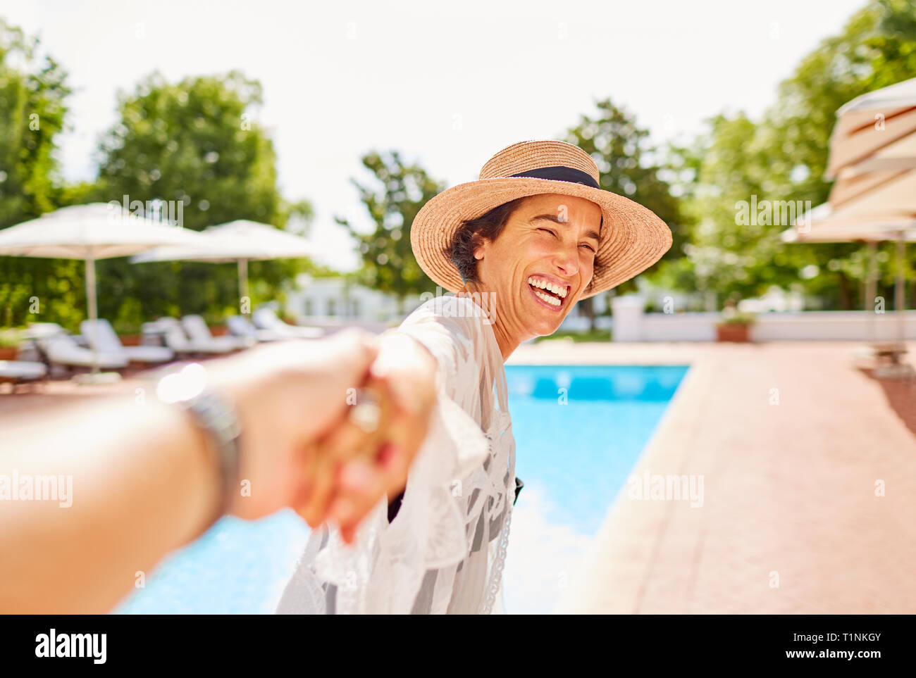 Happy wife leading husband by the hand at sunny resort poolside Stock Photo