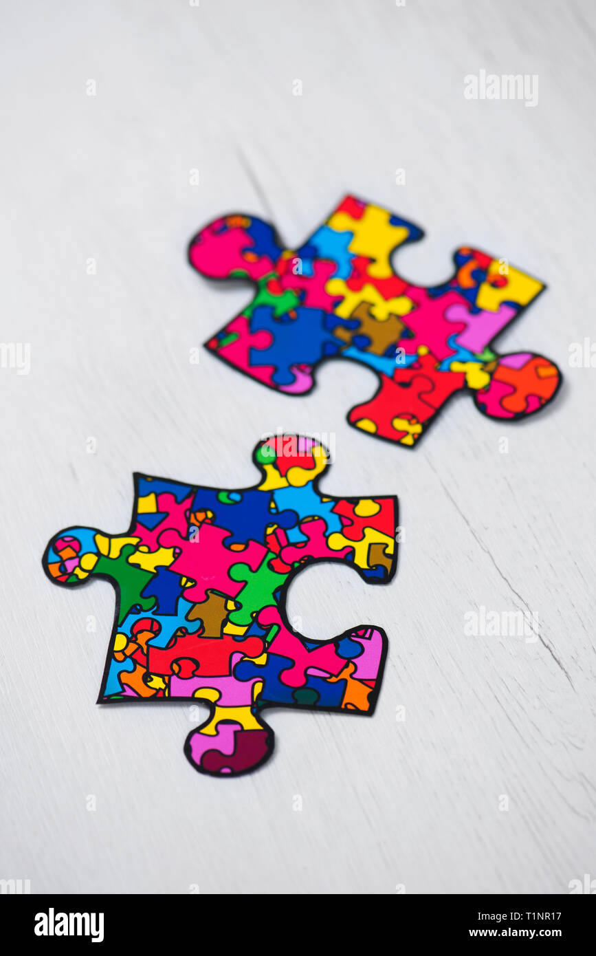 two puzzle pieces patterned with many puzzle pieces of different colors, symbol of the autism awareness, on a white rustic wooden background Stock Photo