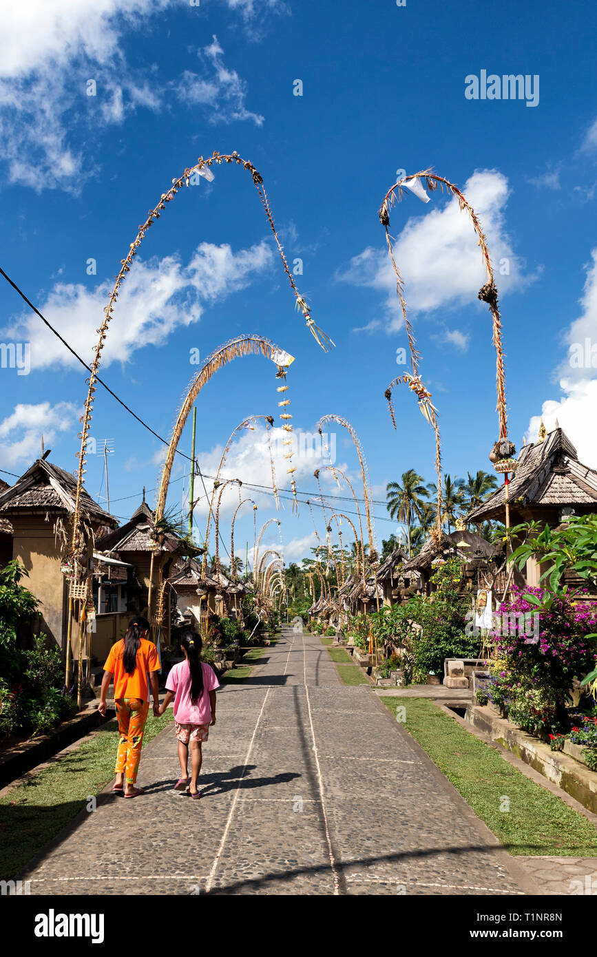Two girls walking around Penglipuran Village (decorated with penjor, curved poles with offerings to celebrate Galungan - the victory of good over evil Stock Photo