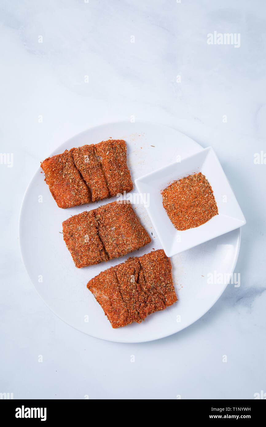 Raw spiced cod fish filets with a spice rub on a white plate. Fresh fish with Mediterranean spices on a white plate and a white marble background. Stock Photo