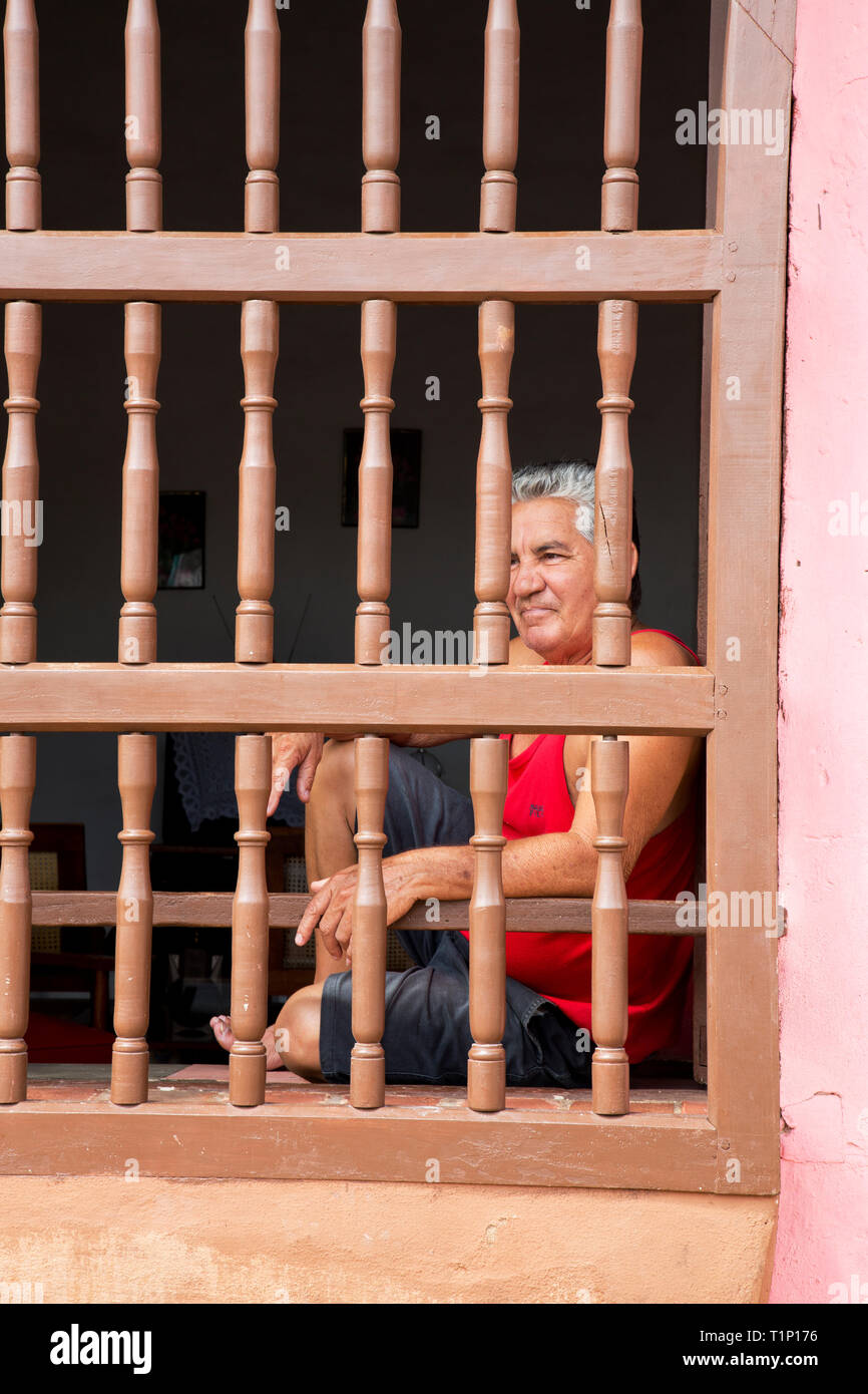 Portrait of a Cuban man, in Trinidad,Sancti Spiritus,Cuba. Street scene showing man relaxing behind a painted wood security screen Stock Photo