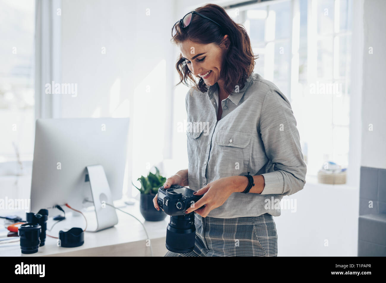Female photographer working in her office. Woman photographer checking pictures on camera and smiling. Stock Photo