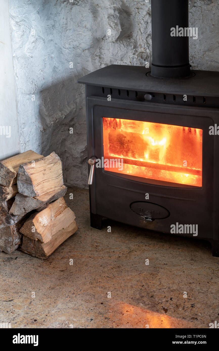 Wood burning in a woodburning stove with a pile of logs. Scotland Stock Photo