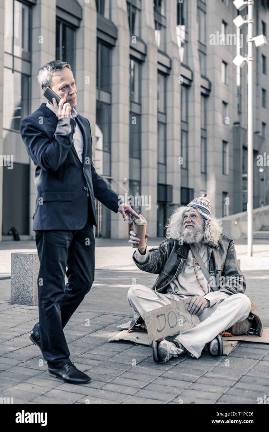 Indifferent rich man talking on smartphone and sharing money with homeless Stock Photo
