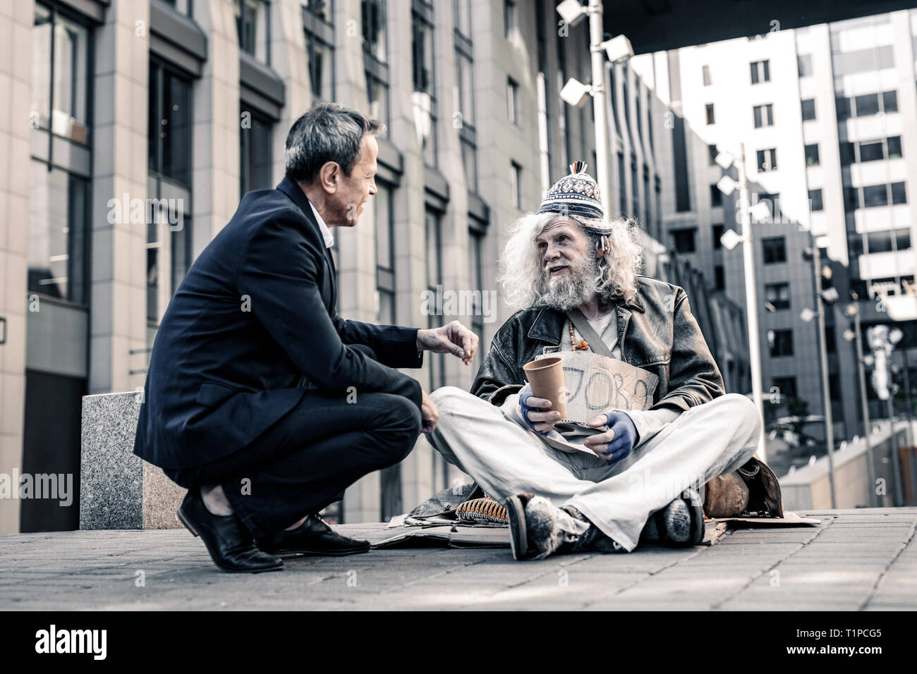 Short-haired man in dark costume being extremely kind to senior homeless Stock Photo