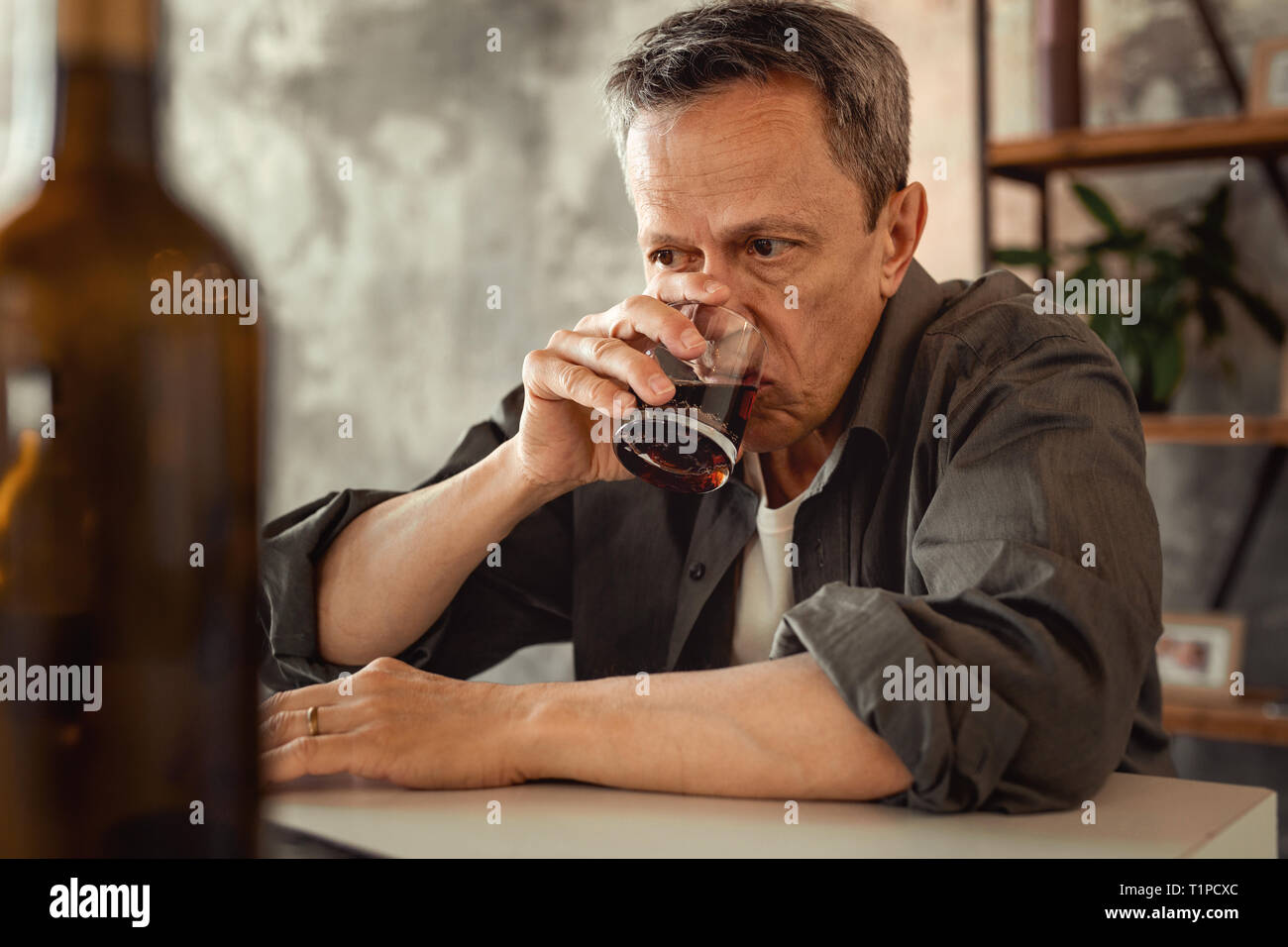 Apathetic grey-haired man sipping alcohol from glass Stock Photo