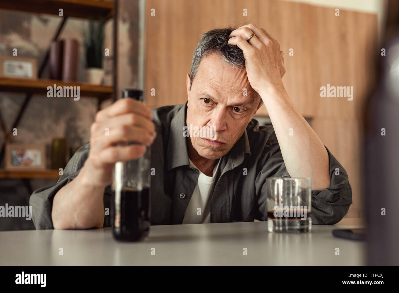 Apathetic short-haired man leaning on his hand and carrying partly-empty bottle Stock Photo