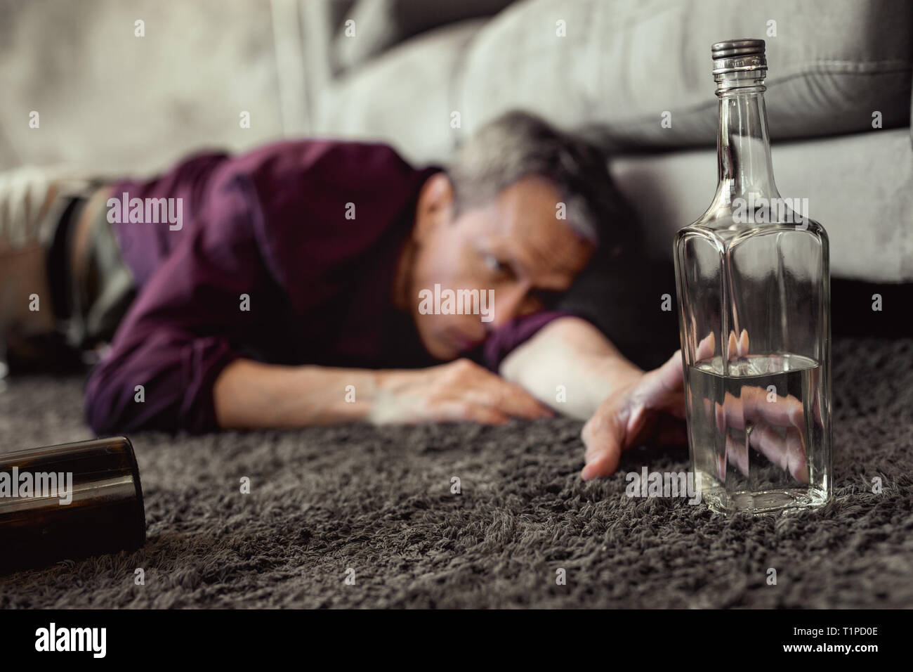 Desperate pity adult man reaching out for half-empty bottle of vodka Stock Photo