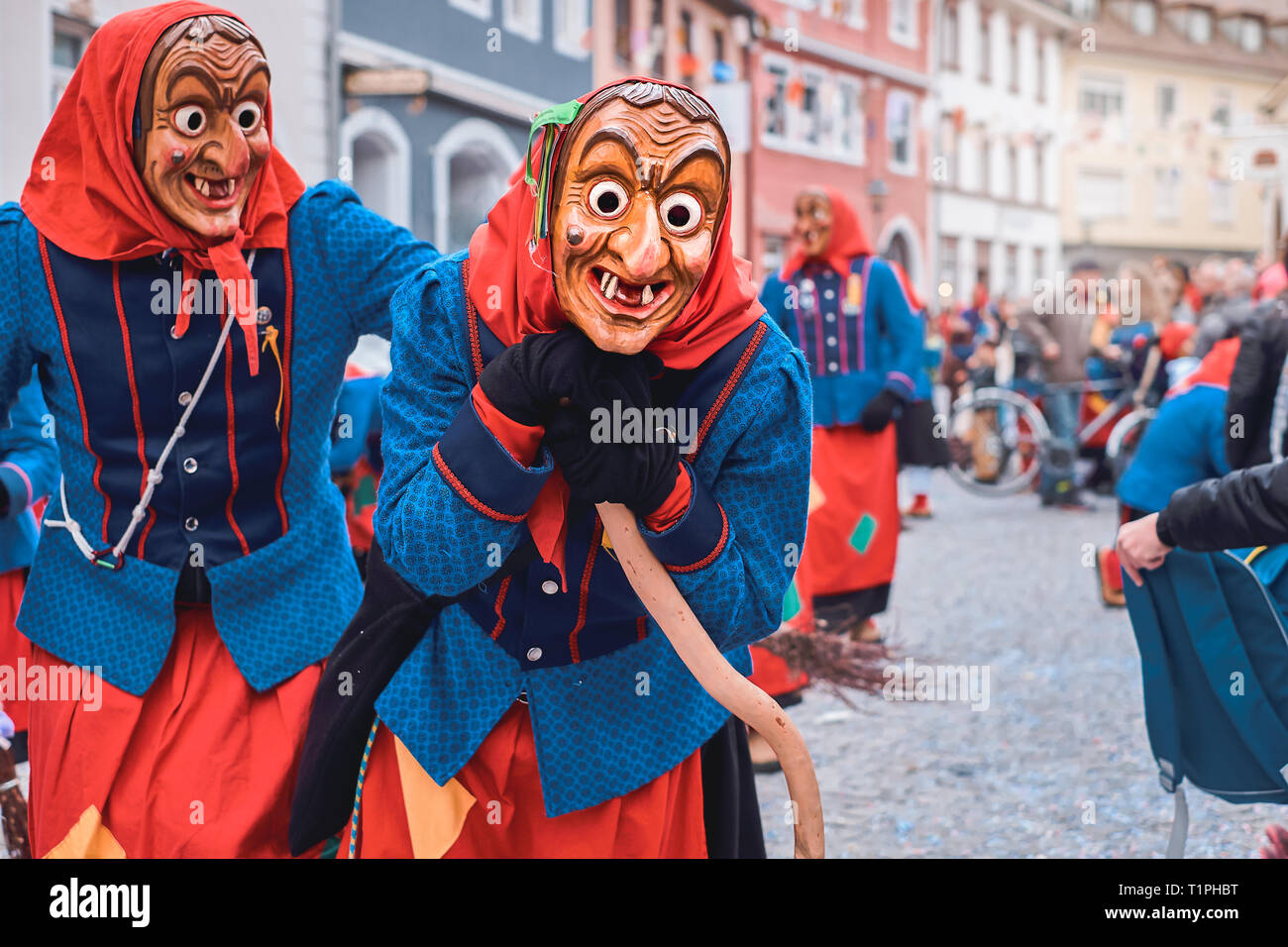 Funny witch in blue red robe is leaning on the broom, another witch is ...