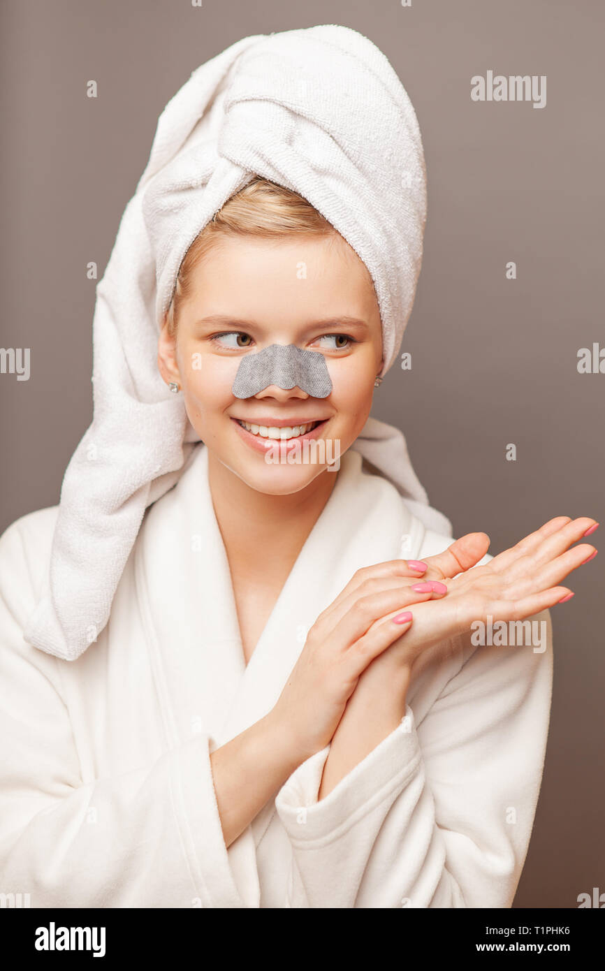 Young woman with fresh healthy skin and hairs aplying stripe from black dots. Cosmetology, beauty and spa. Grey background, Stock Photo