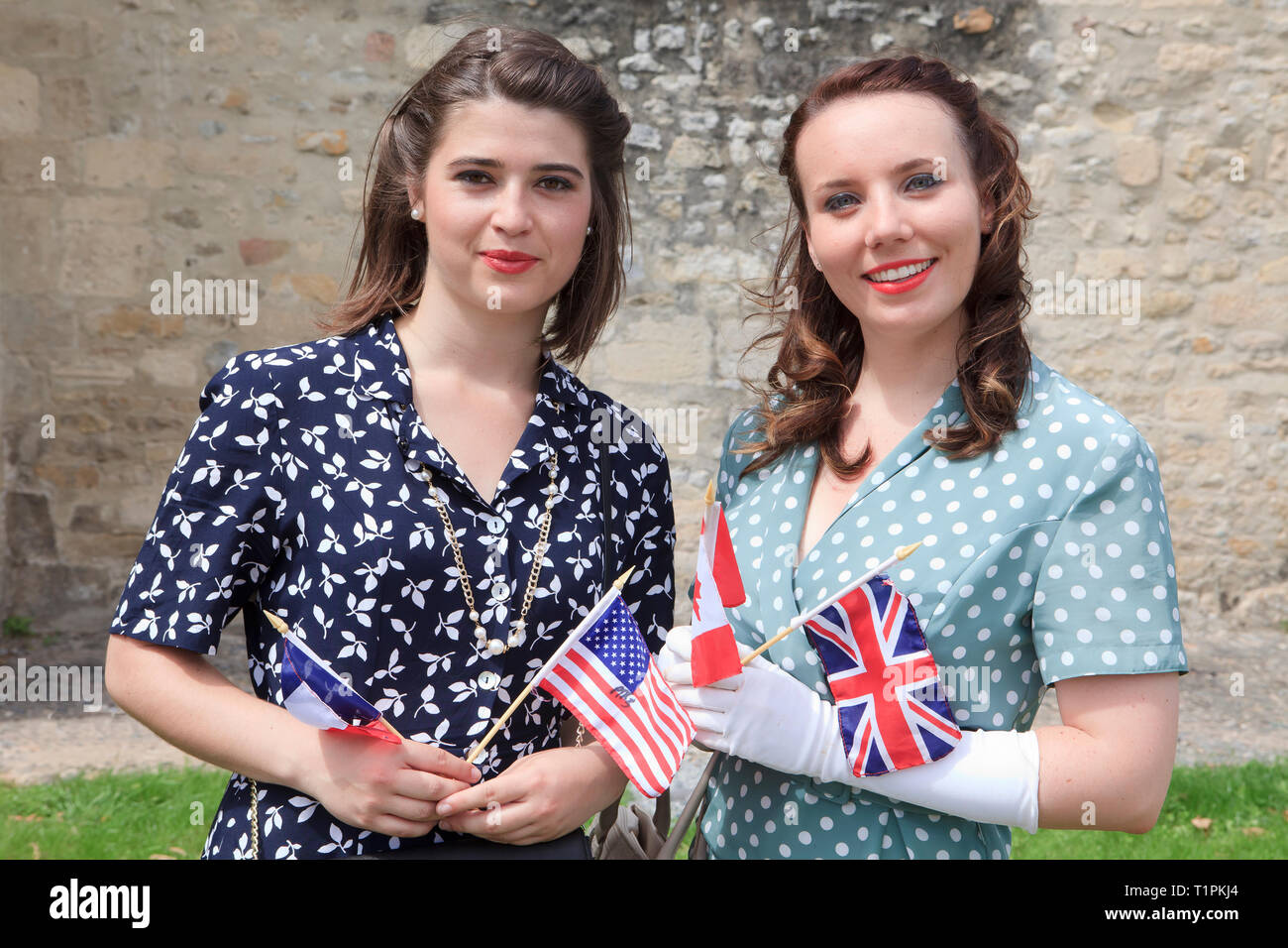 2 young ladies celebrating victory holding flags of the liberating nations France, USA, Canada and the UK in Sainte-Mere-Eglise (Normandy), France Stock Photo