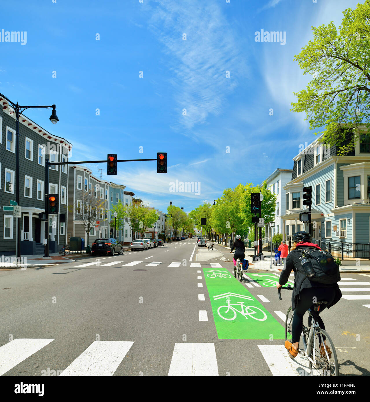 Protected bike lane between parking lane and sidewalk on city street. Bikers conmuting on nice spring day. Stock Photo