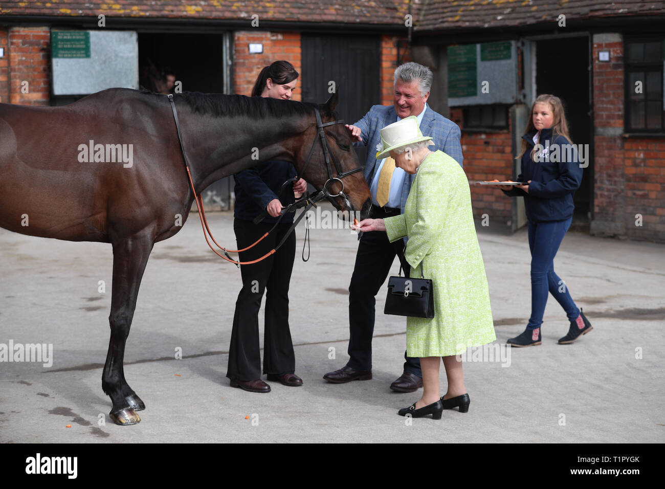 Queen Elizabeth II with trainer Paul Nicholls feeding carrots to a