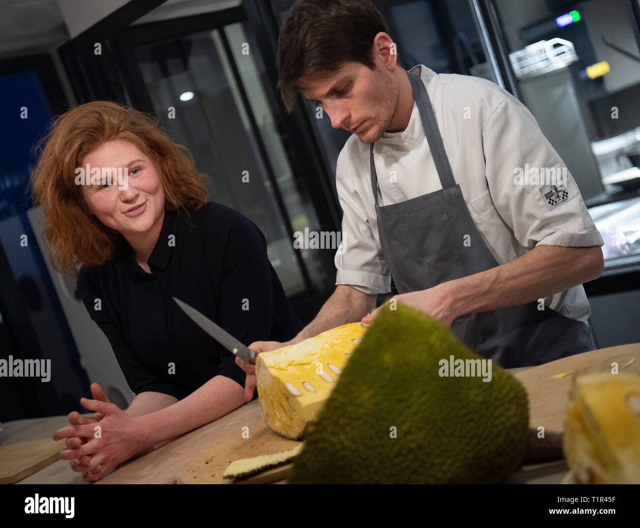 Berlin, Germany. 26th Mar, 2019. A cook opens a jackfruit at a press dinner to introduce jackfruit dishes in the restaurant 'Hermann's'. On the left is Verena Bahlsen. The 26-year-old great-granddaughter of the founder of the biscuit factory Bahlsen and daughter of Werner Bahlsen, the former managing director of the Hanover biscuit dynasty Bahlsen, has founded a restaurant with a colleague in which Jackfruit burgers are served. (to dpa 'A Bahlsen and the Jackfruit') Credit: Monika Skolimowska/dpa-Zentralbild/dpa/Alamy Live News Stock Photo