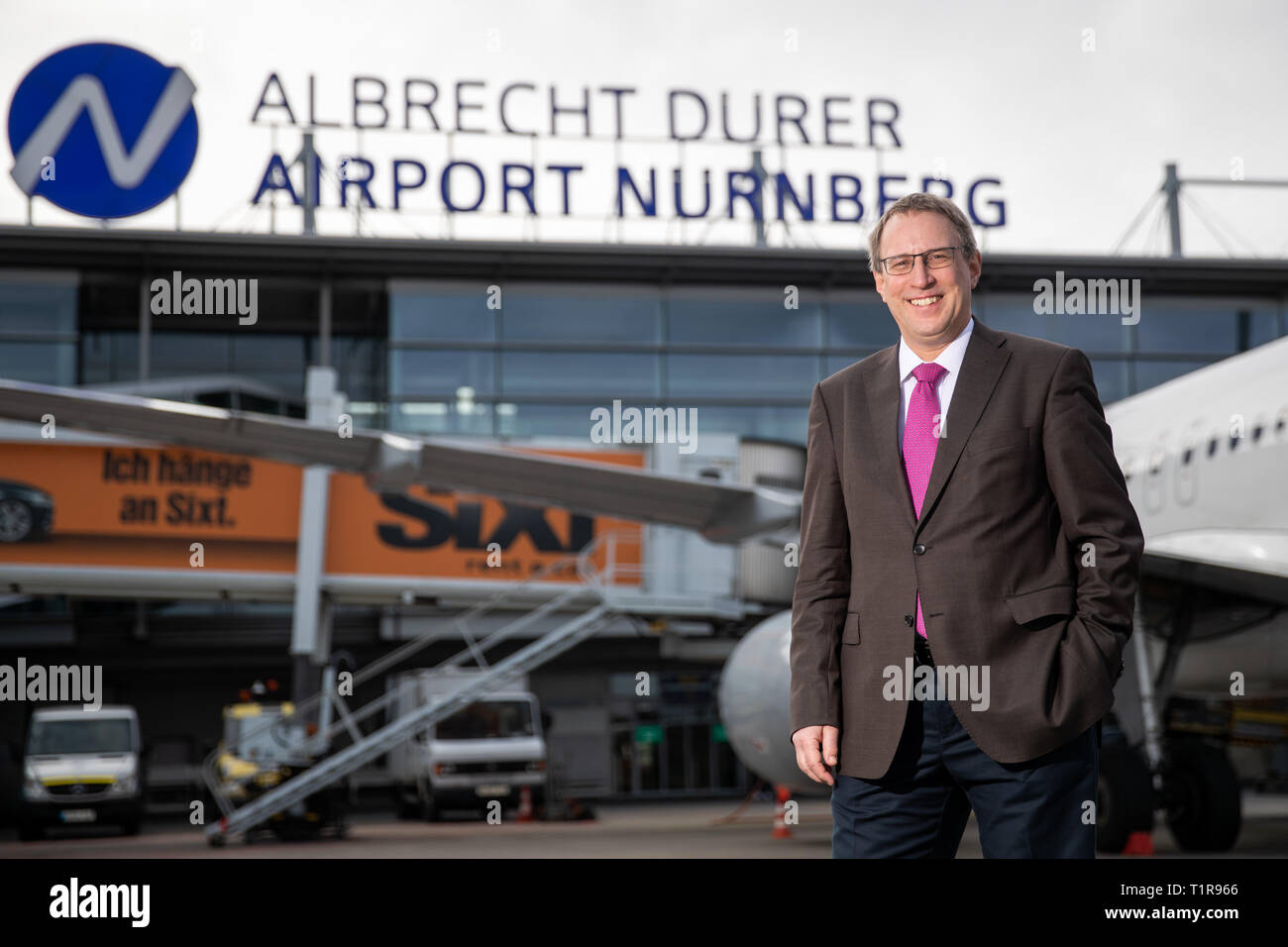 28 March 2019, Bavaria, Nürnberg: Michael Hupe, Managing Director of Albrecht Dürer Airport Nuremberg, stands on the edge of the annual parking lot on the apron in front of the company's logo. Photo: Daniel Karmann/dpa Stock Photo