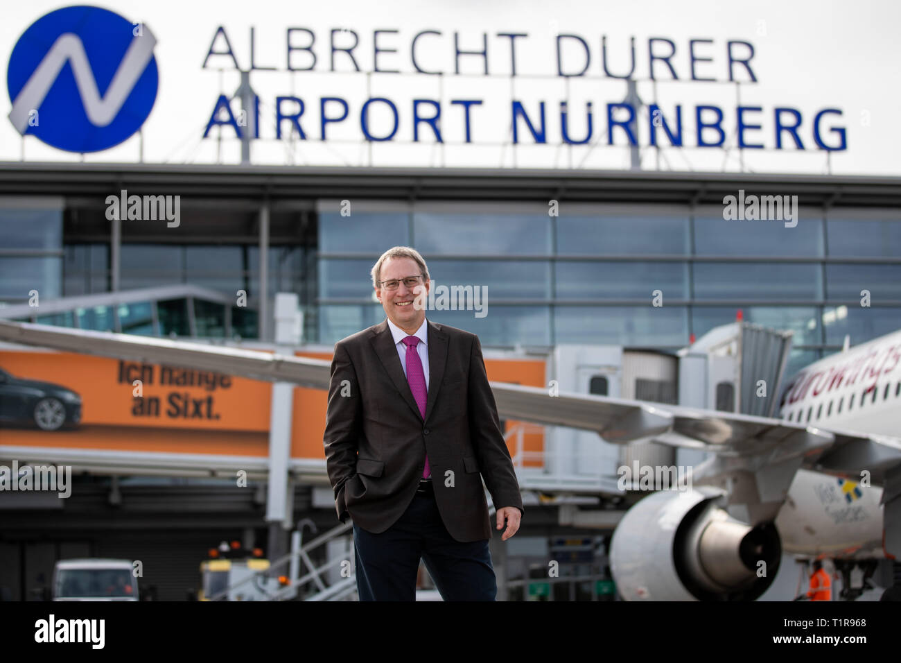 28 March 2019, Bavaria, Nürnberg: Michael Hupe, Managing Director of Albrecht Dürer Airport Nuremberg, stands on the edge of the annual parking lot on the apron in front of the company logo. Photo: Daniel Karmann/dpa Stock Photo