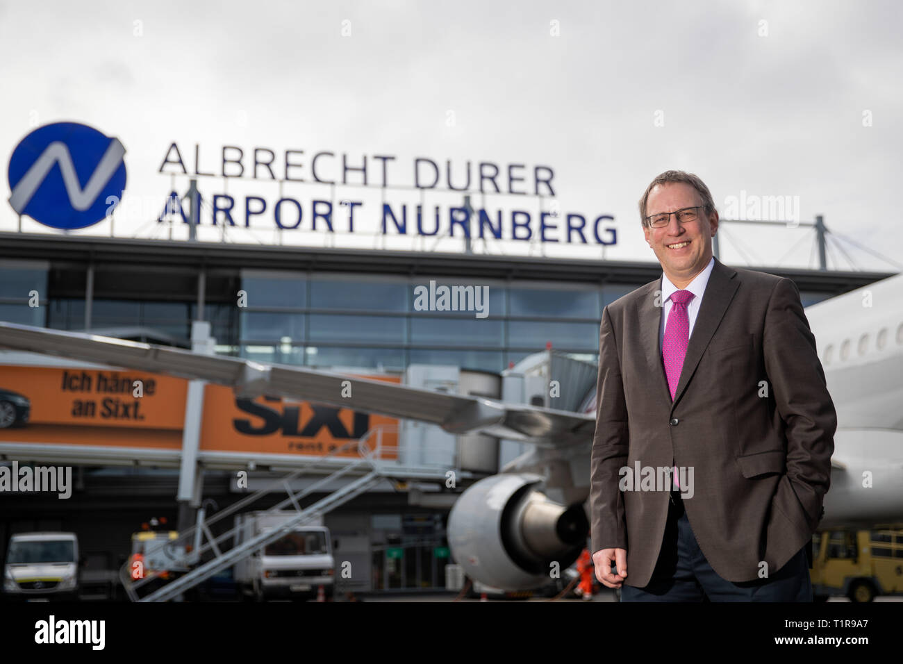 28 March 2019, Bavaria, Nürnberg: Michael Hupe, Managing Director of Albrecht Dürer Airport Nuremberg, stands on the edge of the annual parking lot on the apron in front of the company logo. Photo: Daniel Karmann/dpa Stock Photo