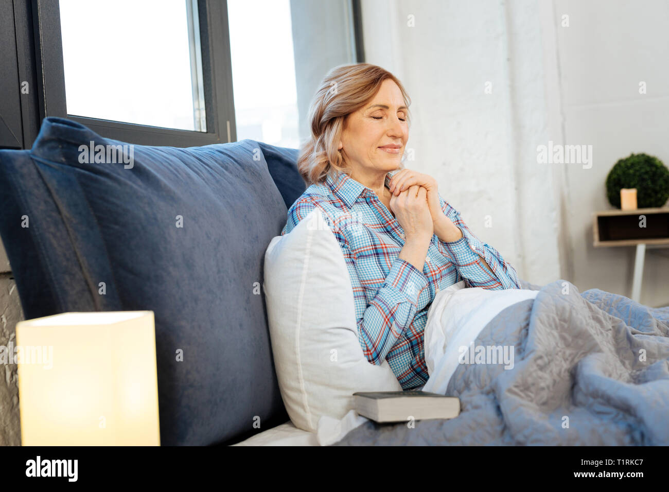 Pleasant calm mature lady holding connected hands in front of her Stock Photo