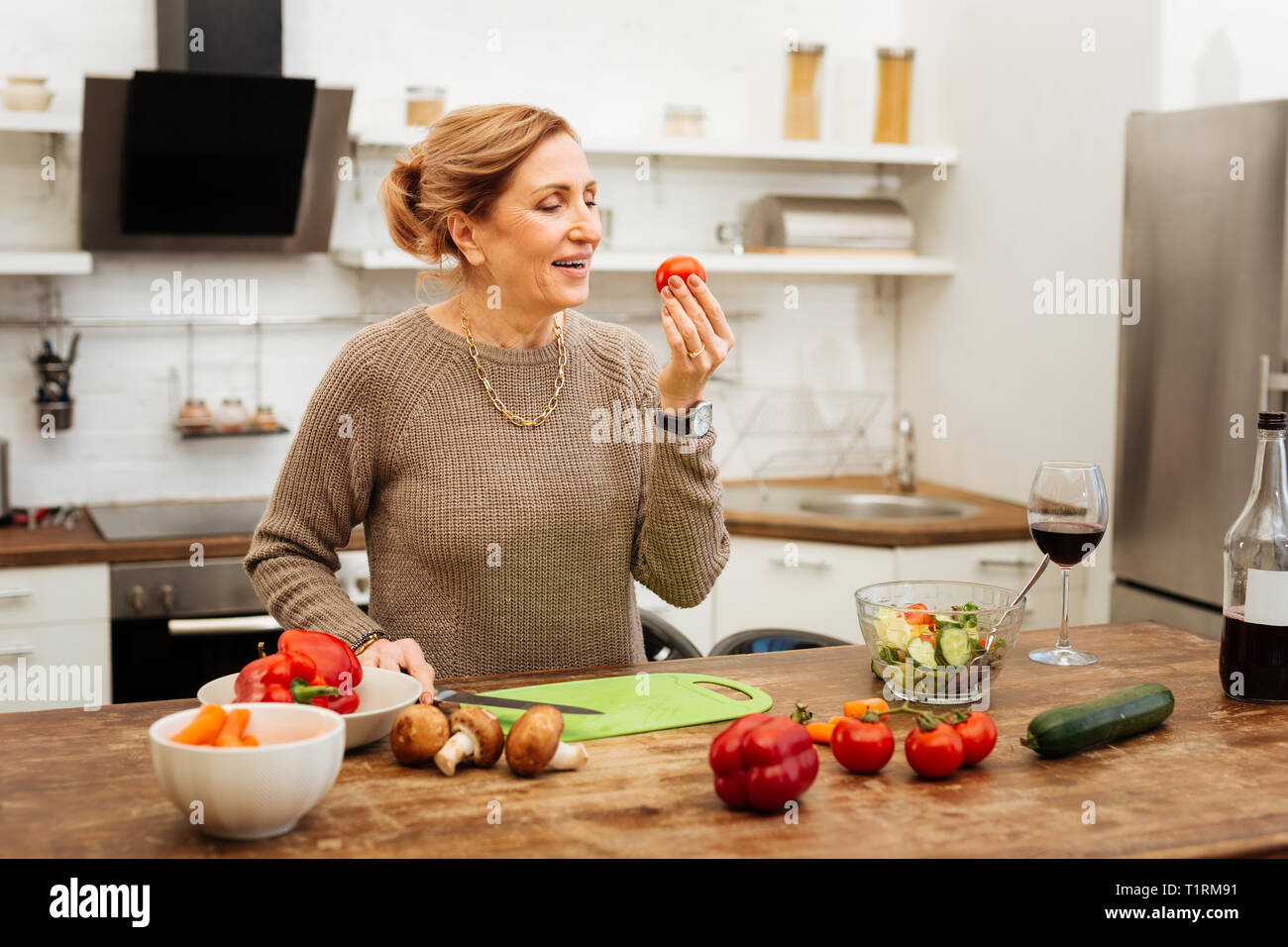 Positive woman with tied hair observing tomato in her hand Stock Photo