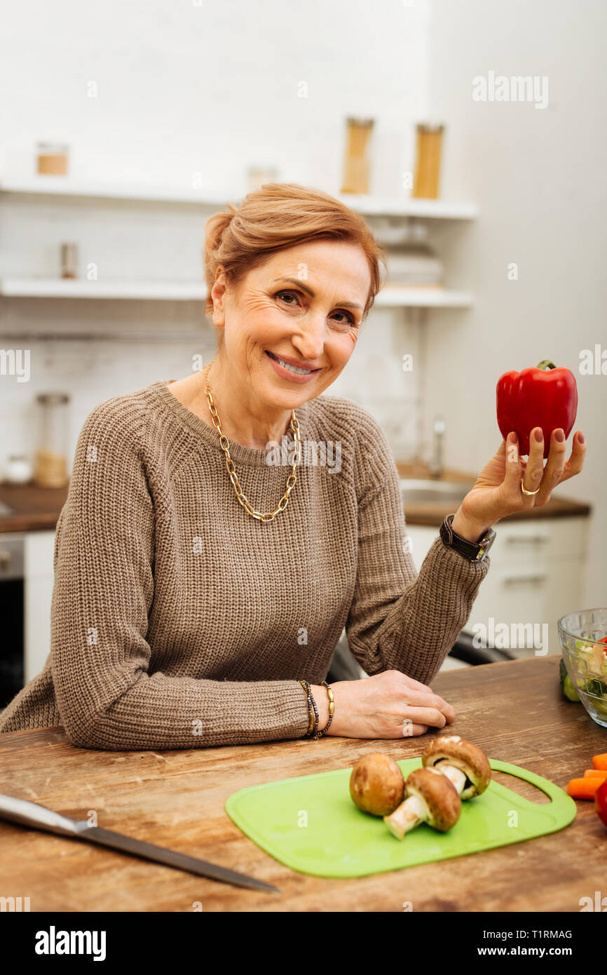 Joyful appealing adult lady wearing beige sweater and carrying red pepper Stock Photo