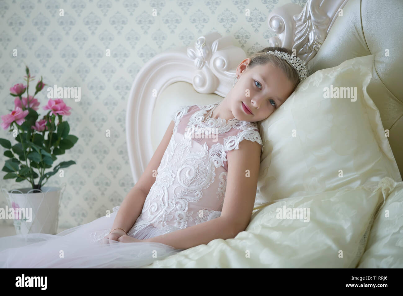 Cute tender girl teenager lies on the bed. Princess in a white dress with a crown. Stock Photo