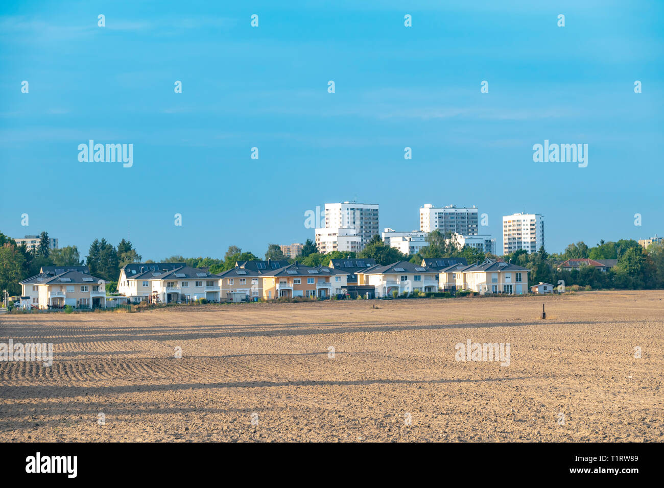 View over a harvested field and small houses to the satellite city Gropiusstadt in Berlin-Neukoelln illuminated by the sun. Stock Photo